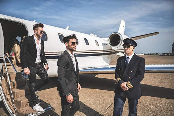 Nicely dressed celebrity people with sunglasses exiting the private jet airplane. The pilot stands to escort them.